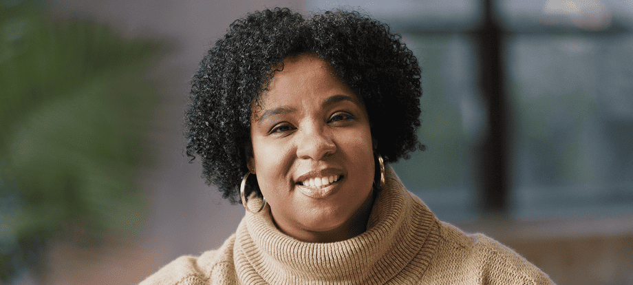 QULIPTA® patient Latoya wearing a brown sweater and smiling after sharing her migraine preventive journey.